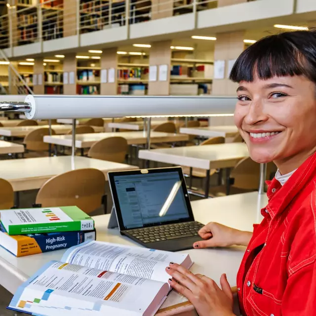 Eine Studentin sitzt an einem Arbeitsplatz in der Hochschulbibliothek mit Büchern und einem Notebook