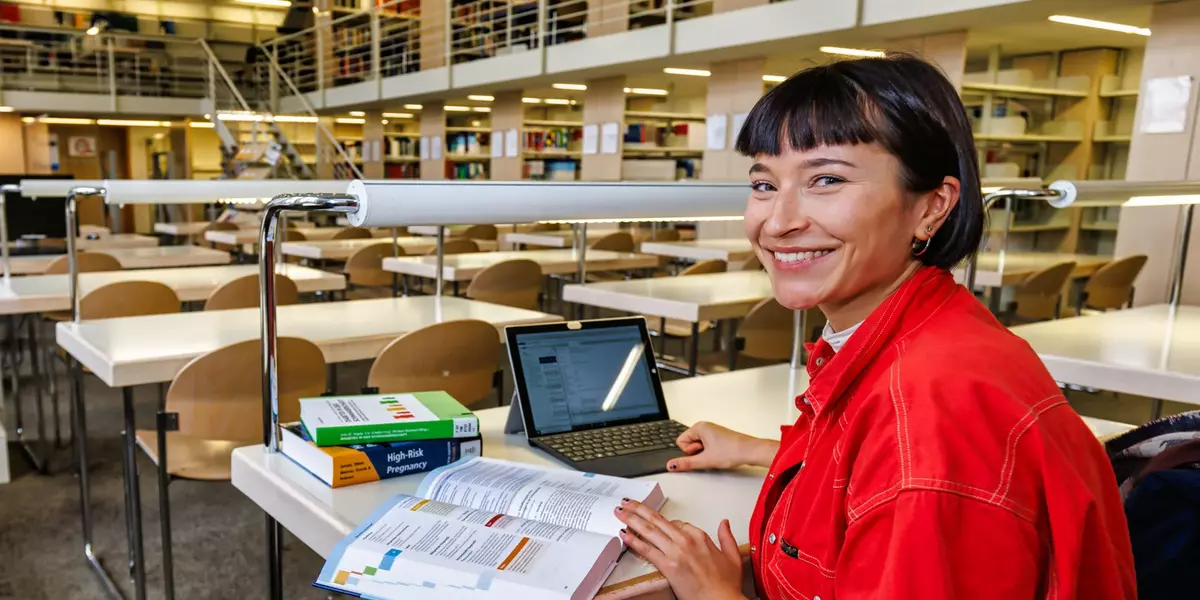 Eine Studentin sitzt an einem Arbeitsplatz in der Hochschulbibliothek mit Büchern und einem Notebook