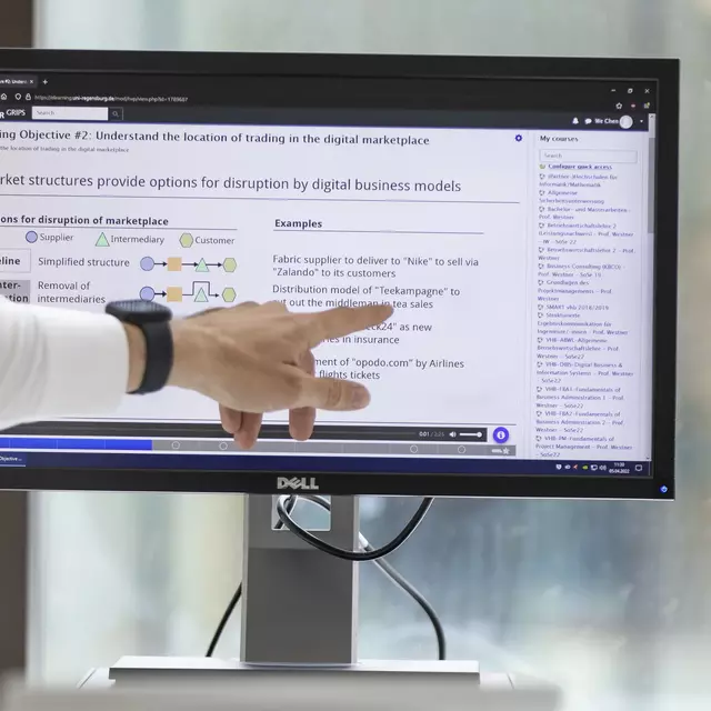 A man in a white shirt points to a screen and explains something to a young employee.