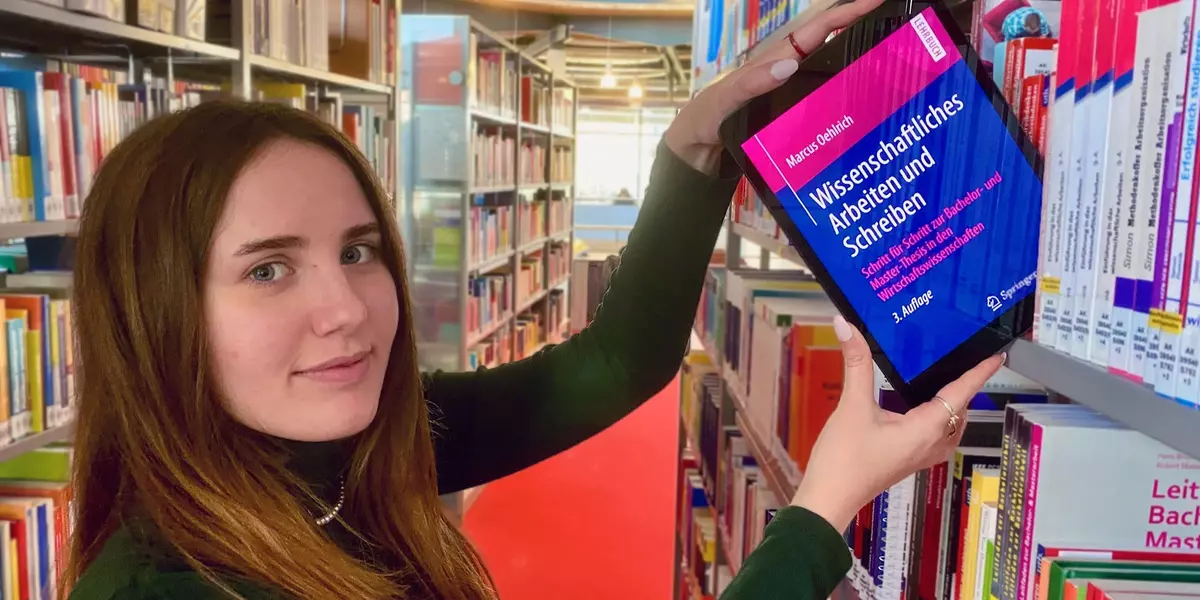 Studentin zieht ein iPad mit geöffnetem E-Book aus einem Bücherregal