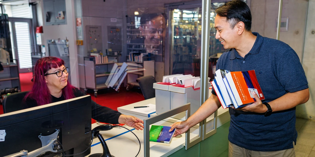 Student leiht ein Buch an der Ausleihtheke aus