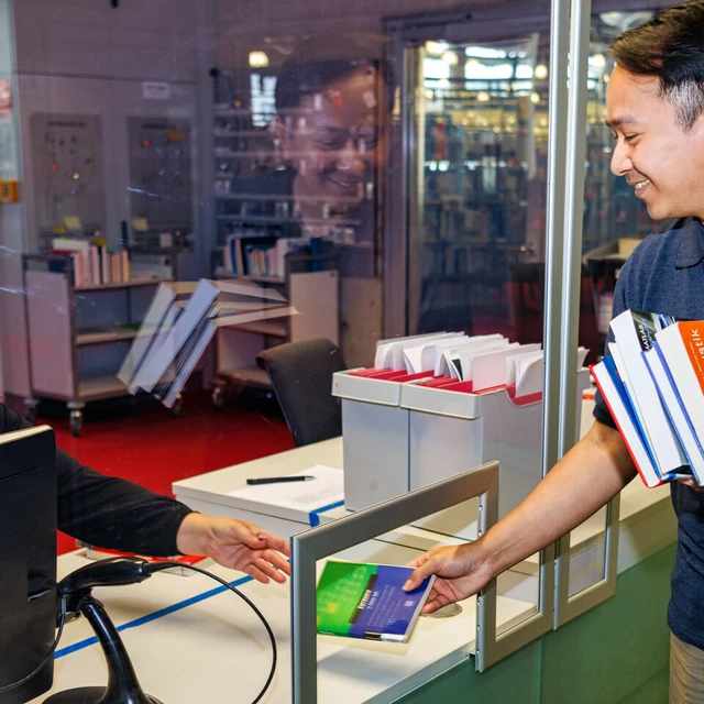 Student leiht ein Buch an der Ausleihtheke aus