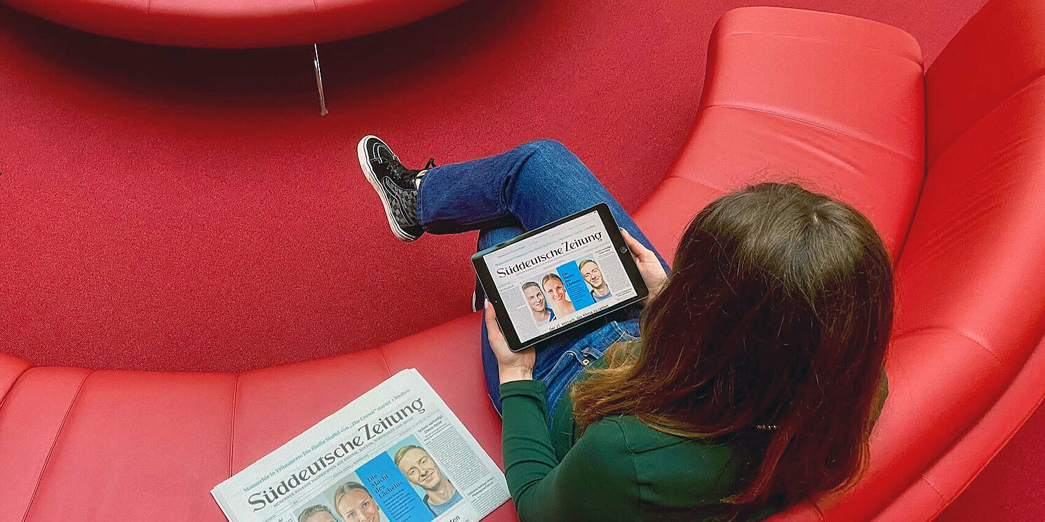Studentin liest eine Online-Zeitung auf einem roten Sofa