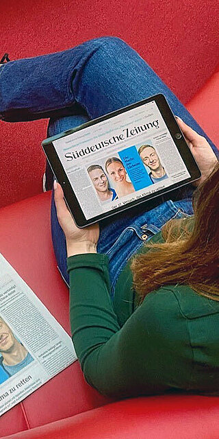 Studentin liest eine Online-Zeitung auf einem roten Sofa