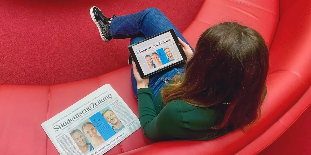Studentin liest eine Online-Zeitung auf einem roten Sofa